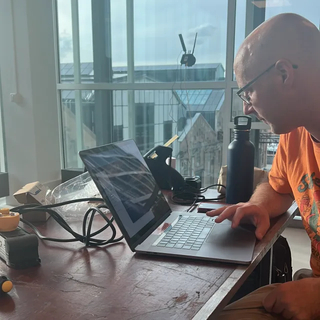 Working on a laptop at a table with hardware and tools
